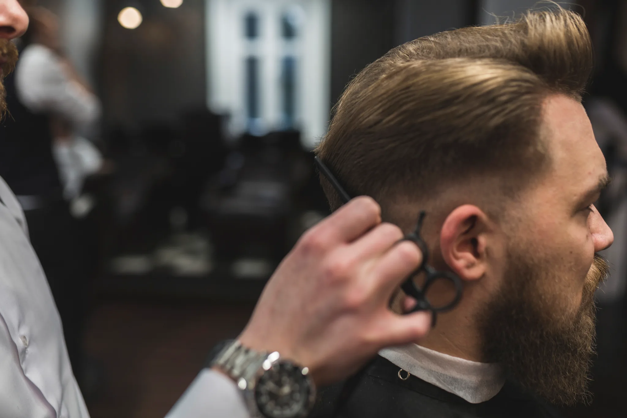 Frizer tunde cu foarfeca un bărbat cu barbă în salonul de frizerie Magic